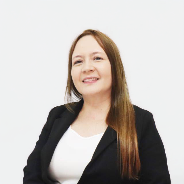 A woman with long brown hair wearing a black blazer and a white shirt, smiling against a plain white background.